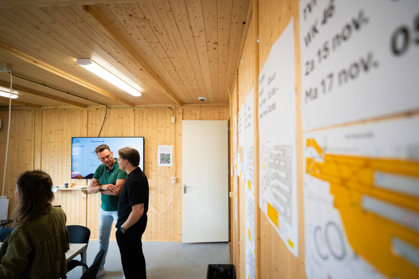 Kennisdelen in een bouwkeet met collega's op een whiteboard en langs de muur