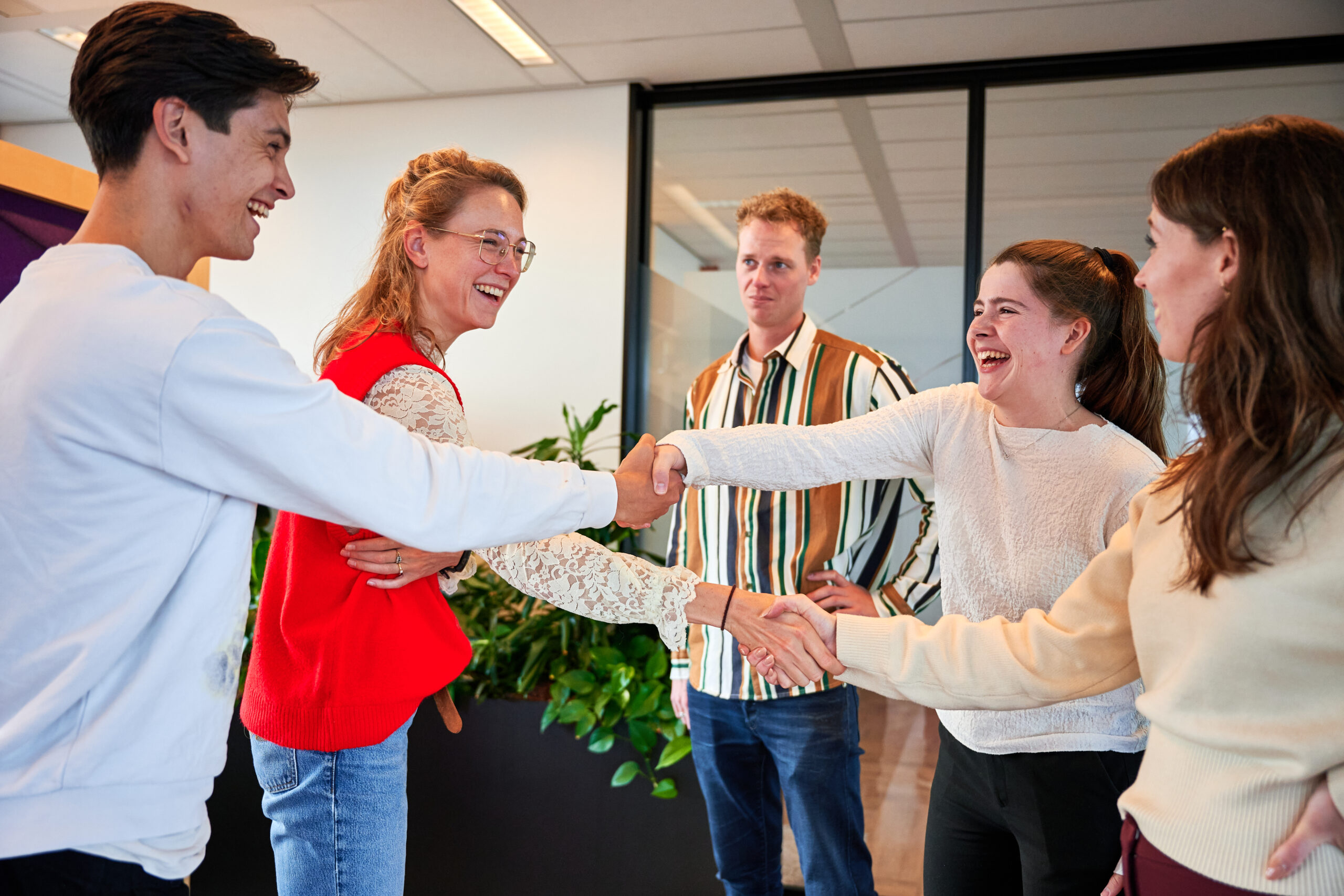 Collega's op kantoor – grote groep mensen zijn druk in gesprek met elkaar – mensen geven elkaar een hand (zelfde context als vorige foto’s)>