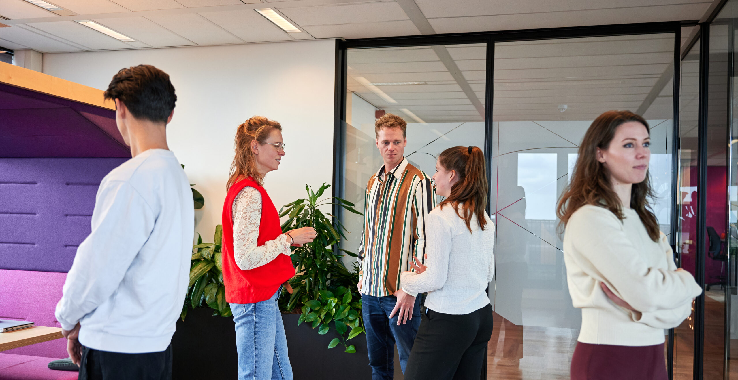 Collega's op kantoor – grote groep mensen zijn druk in gesprek met elkaar en er staan 2 mensen buiten de groep (zelfde context als vorige foto’s)>